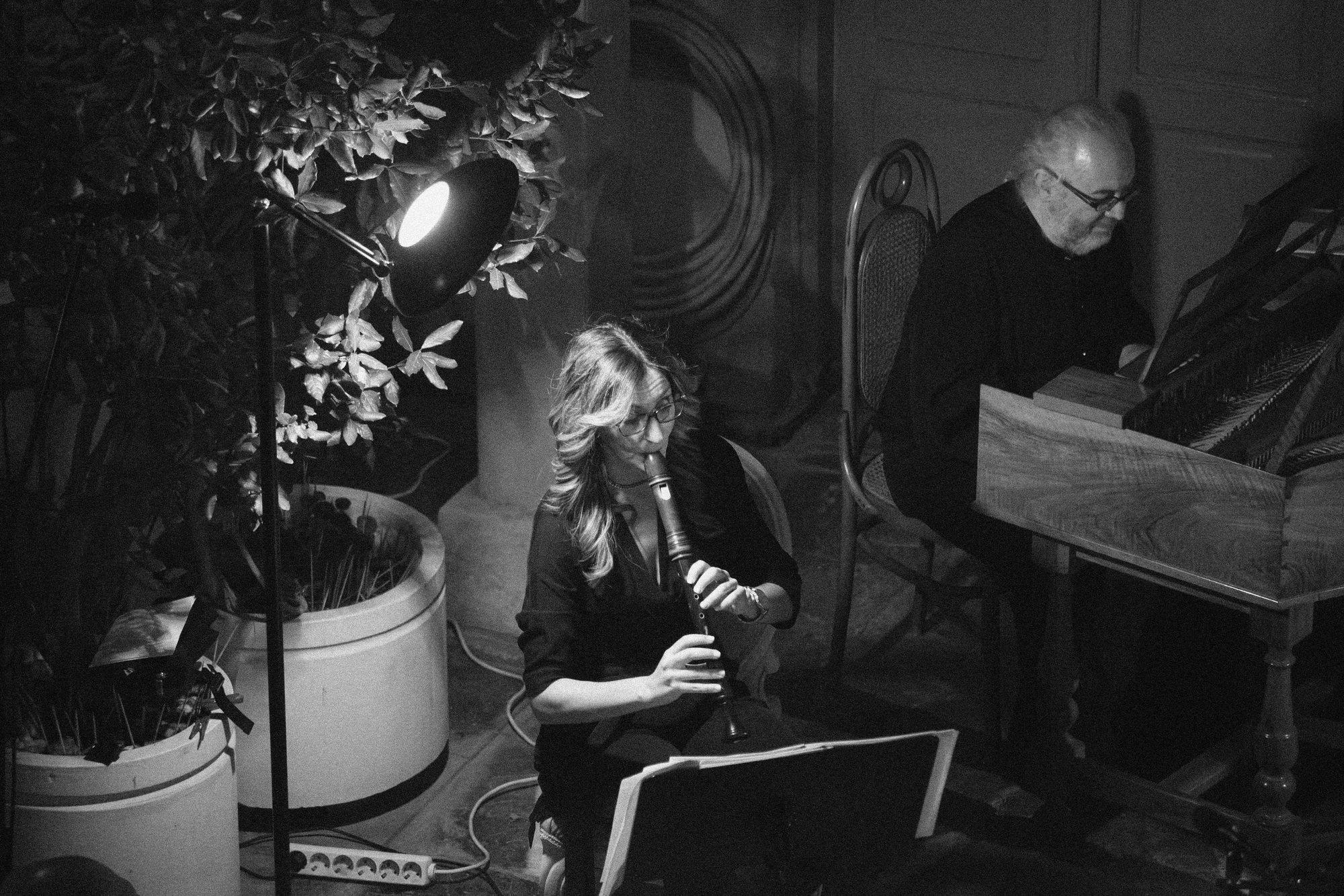 A recorder player and a harpsichordist performing by the light of a single stage lamp.