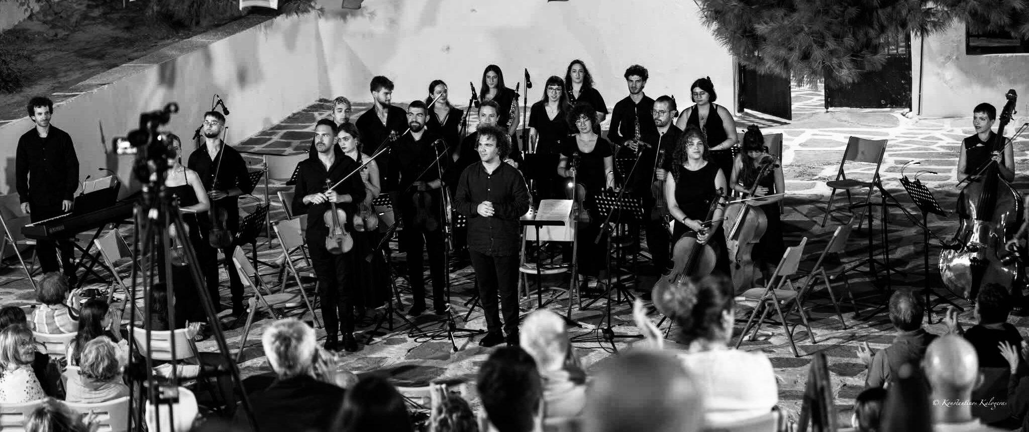 Singers and instrumentalists standing together in an open-air square at night.
