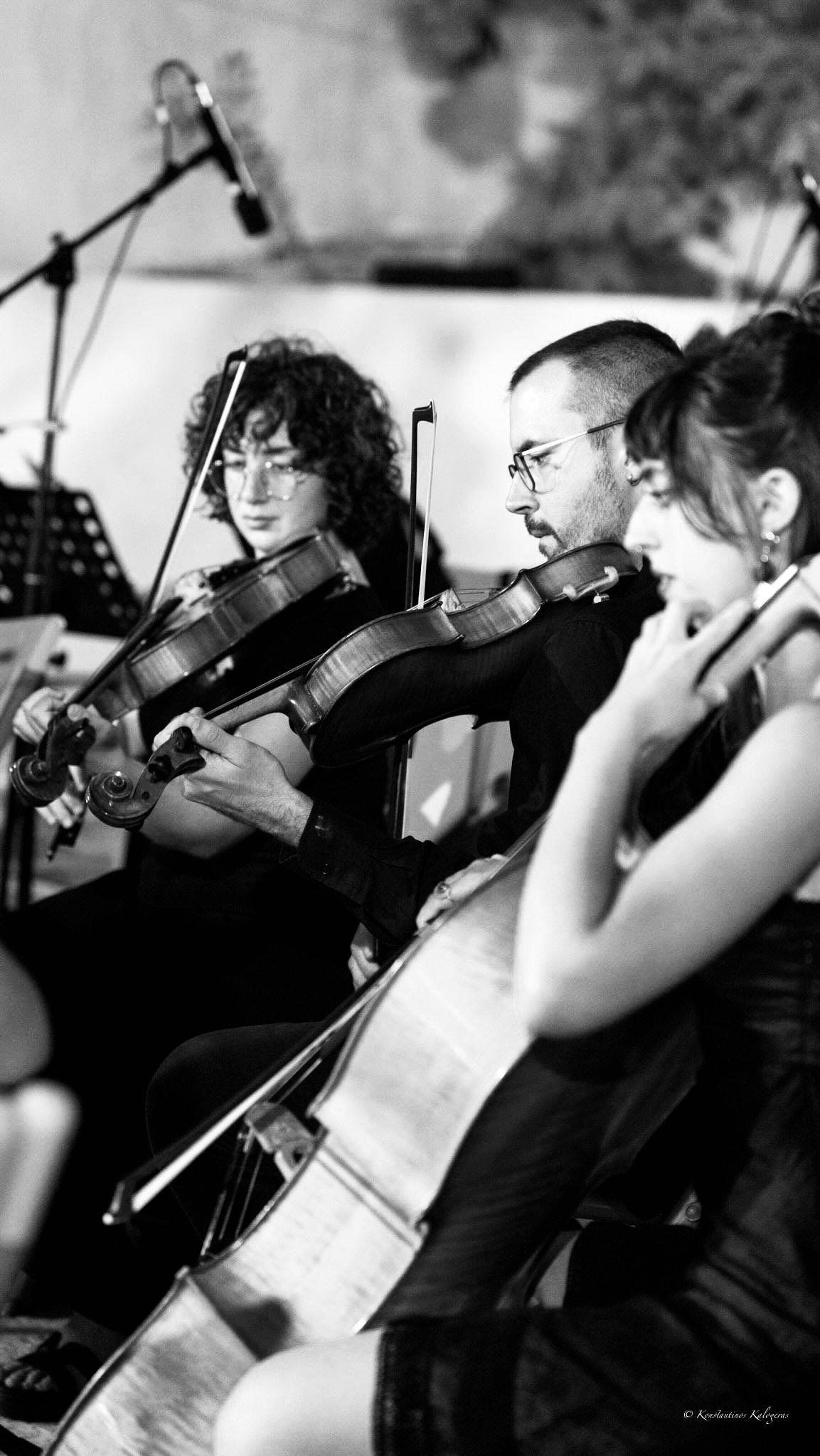 Violinists and a cellist playing close together, a microphone above them.