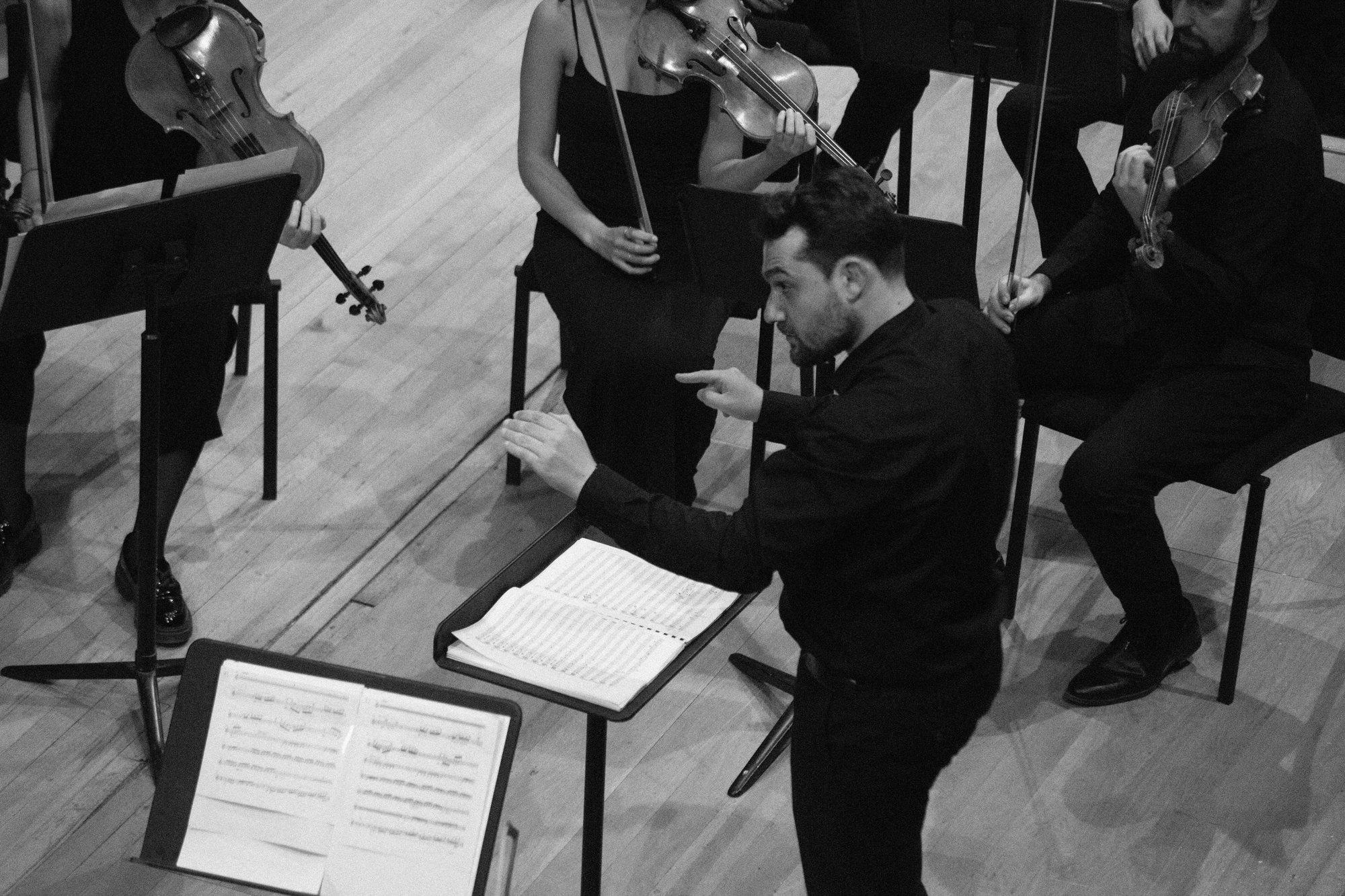 Seen from above, the conductor points towards the violins between two music stands with open parts.