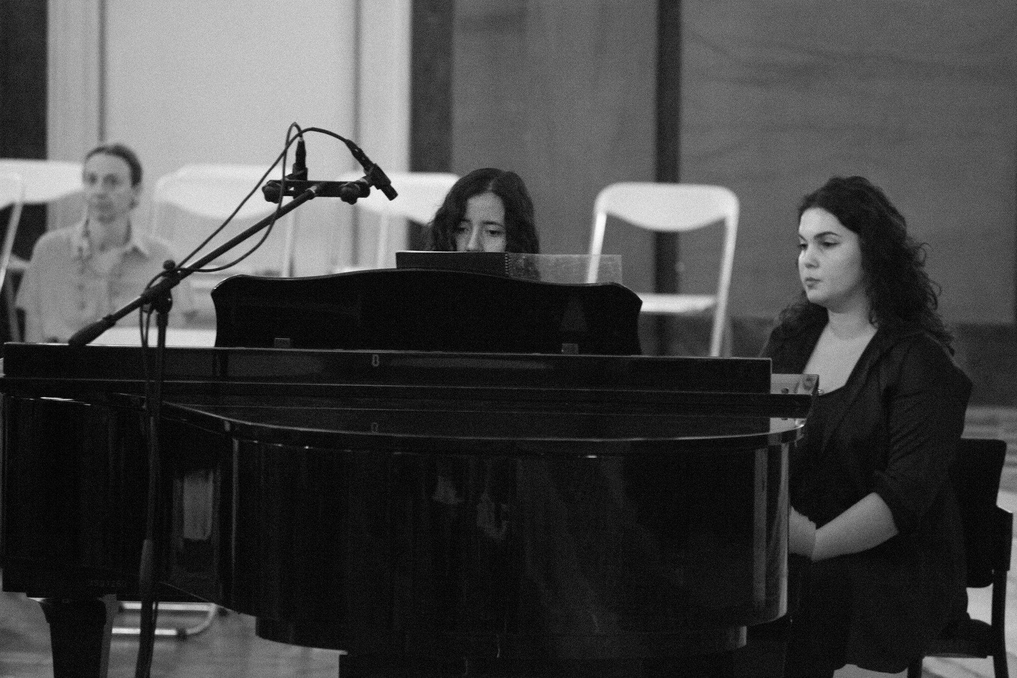 Deux femmes au piano à queue, l’une joue, l’autre écoute, devant le public.
