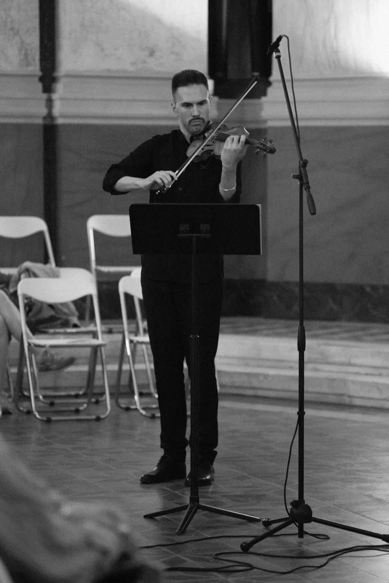 A violinist standing at a music stand in the marble hall, playing.