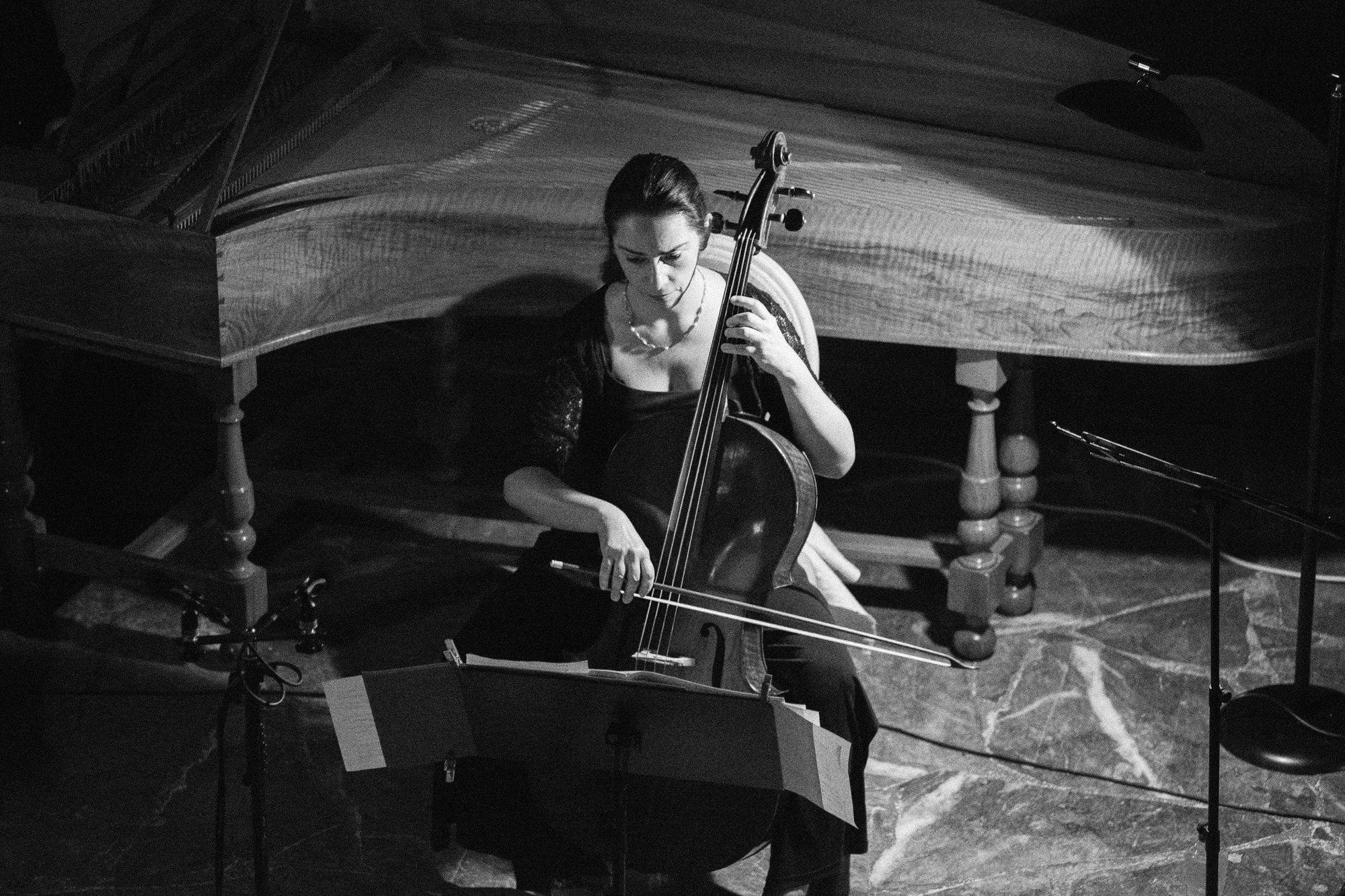 Un violoncelliste assis devant le clavecin, vu d’en haut.