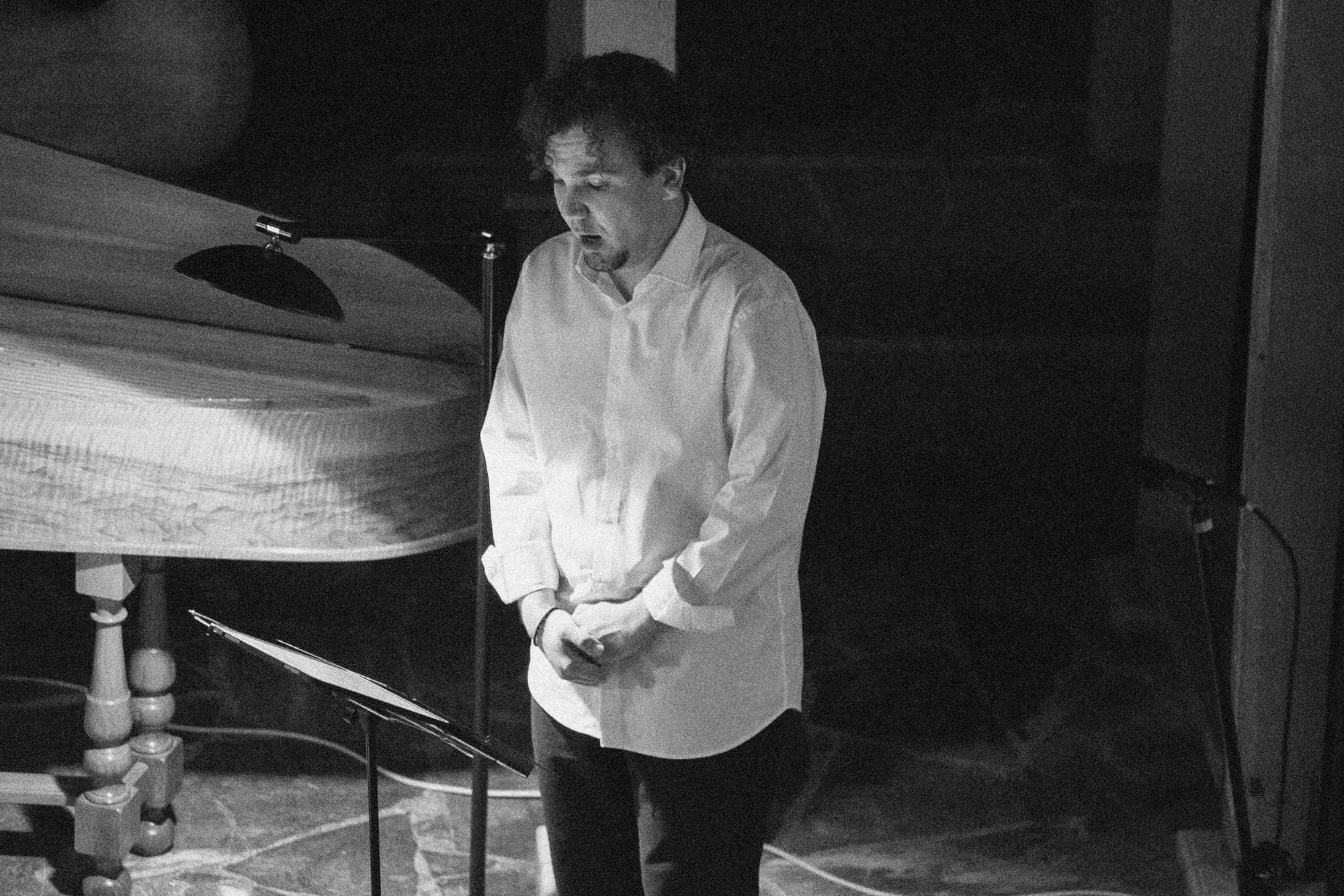 Un chanteur en chemise blanche, debout près du clavecin, en train de chanter.
